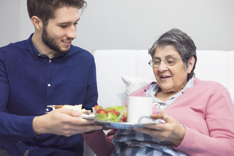 male caregiver helping older female with food tray Someren Glen Senior Living Community in Centennial, CO - male caregiver helping older female with food tray