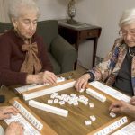 group of happy senior women playing mah-jong with friends