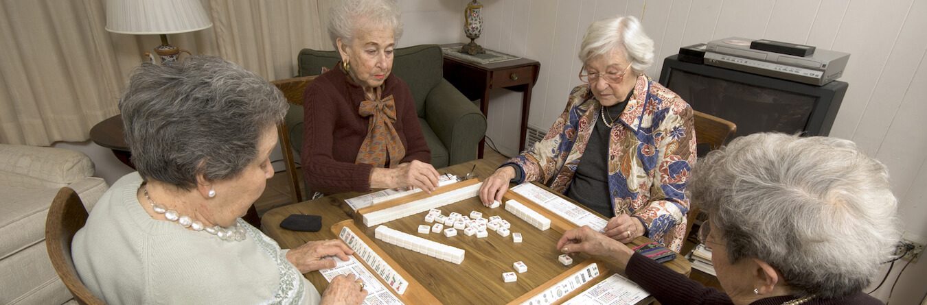 group of happy senior women playing mah-jong with friends