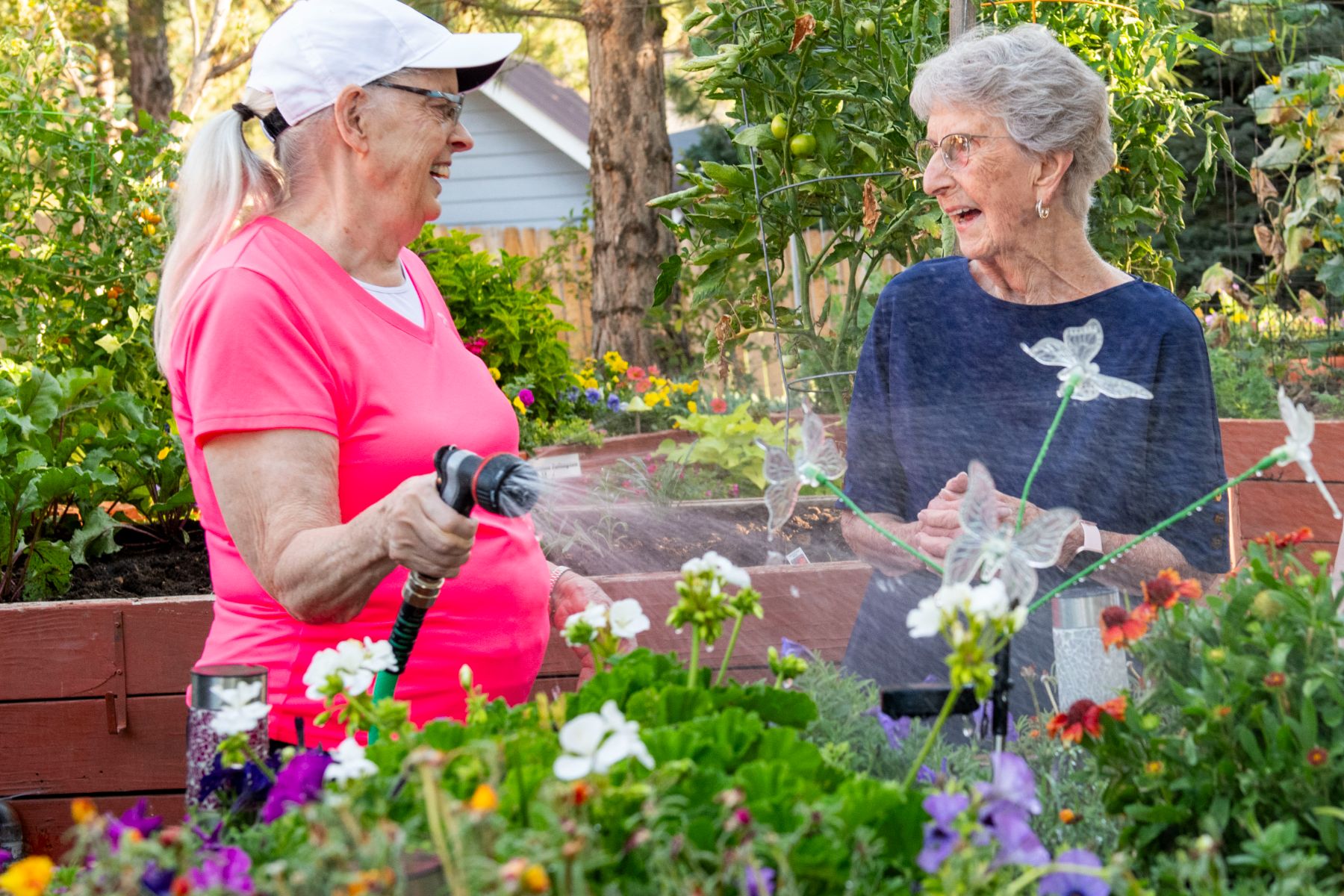 Someren Glen Senior Living Community in Centennial, CO - older woman watering garden bed and talking to friend landscape