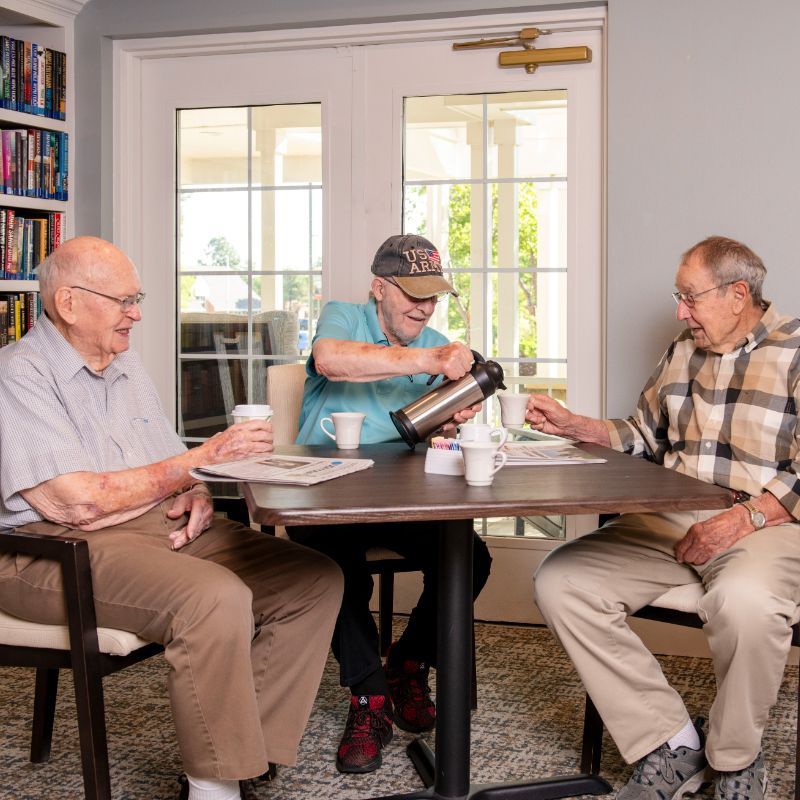 Someren Glen Senior Living Community in Centennial, CO - three older men talking over coffee in library square